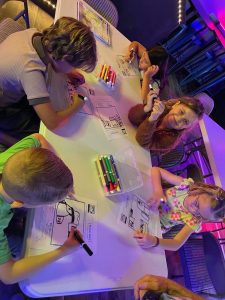 Niños felices se sentaron alrededor de una mesa trabajando en su lección de Escuela Dominical con marcadores.
